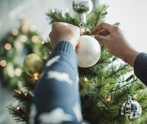 nuori mies viettää joulua kotona ja koristaa joulukuusi kotiin on koristeltu joulukoristeilla ja -valoilla
