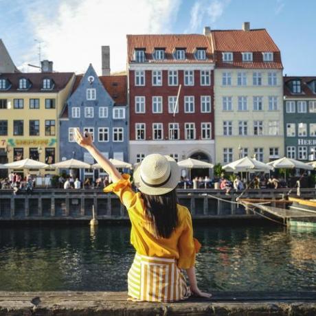 Junge Frau sitzt vor bunten Gebäuden entlang Nyhavn (Neuer Hafen), Kopenhagen, Dänemark