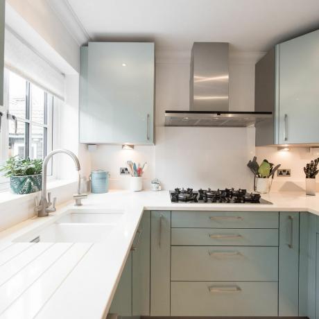 egy modern metálzöld felszerelt konyha általános belső nézete, fehér kvarc munkalappal, alul szerelt mosdóval egy otthonban