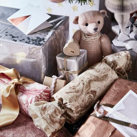 מקרוב של מתנות מתחת לעץ חג המולד, דובי קטן וכסף וזהב עטוף מתנות יקרות מעניקות לאריזת מתנות נופך של זוהר על ידי שימוש בניירות בכסף, נחושת ושיש מסיים