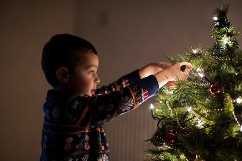 Junge, der zu Hause einen Weihnachtsbaum schmückt