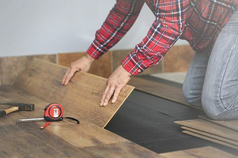 mãos de trabalhador instalando piso laminado de madeira na sala