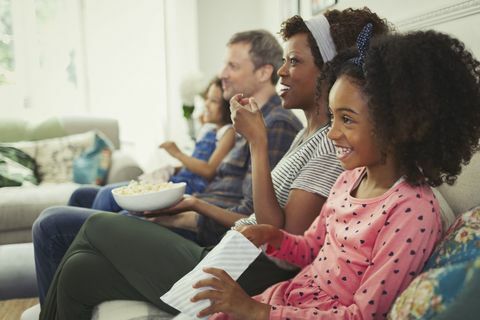 Молодая многонациональная семья смотрит фильм и ест попкорн на диване
