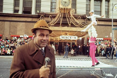 Džo Garagiola runā mikrofonā ar akrobātiem fonā Macy's pateicības dienas parādē 1970. gadā