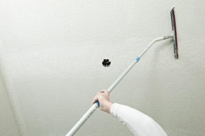 een gipsplaatwerker strijkt met een rubberen mes over opgespoten gipsplaatmodder om een ​​plafond-omlaag-textuur te creëren. De bovenkant van de afbeelding moet nog worden afgevlakt, het midden tot de onderkant is klaar