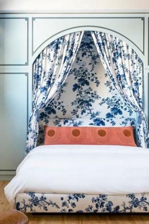 sypialnia z toaletową tapicerką i zasłonami oraz nowoczesną pomarańczową poduszką