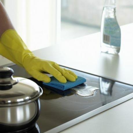 Mâini cu mănuși care curăță o plită cu dezinfectant
