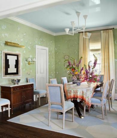 ēdamistaba, zaļas tapetes, zils un balts sešstūra paklājs, balti un zili krēsli, krēmkrāsas aizkari