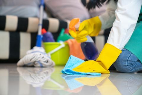 koncept čiščenja in čiščenja moža, srečna mlada ženska v modrih gumijastih rokavicah, ki briše prah s pršilom in brizgalno med čiščenjem na tleh doma