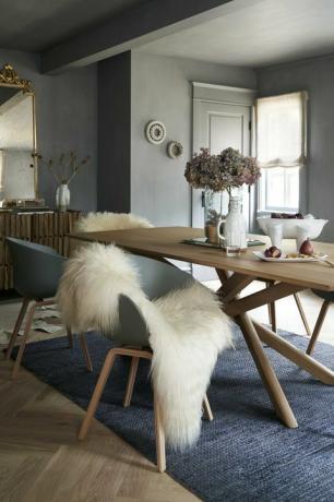 Esszimmer mit blauem Teppich und Holztisch, blauen Stühlen und Schaffellteppich, graue Farbe