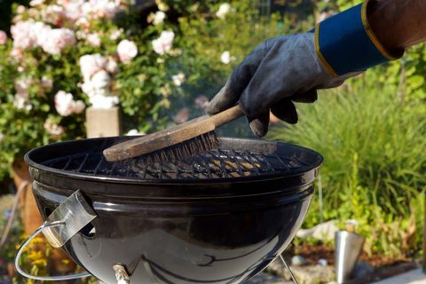 Grillin puhdistus. Miespuolinen käsi käsineineen puhdistaa jäykän harjan pyöreän grillin ennen ruoanlaittoa. hankausvälineet likaisen grillin puhdistamiseen