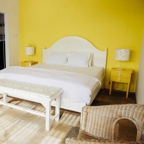Indonēzija, Bali, guļamistaba ar dzeltenu sienu un dzelteniem brīvdienu villas skapīšiem pie gultas