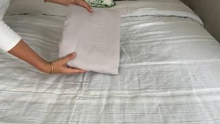 Hände halten gefaltetes Spannbettlaken über dem Bett
