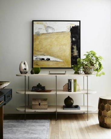 estantería blanca, pila de libros, otomana de oro, arte de la pared, planta en maceta