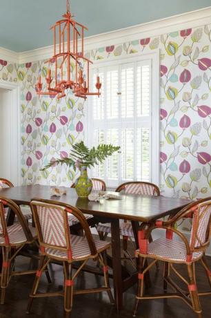 salle à manger avec papier peint fleuri, table en bois et chaises de salle à manger en rotin blanc et orange