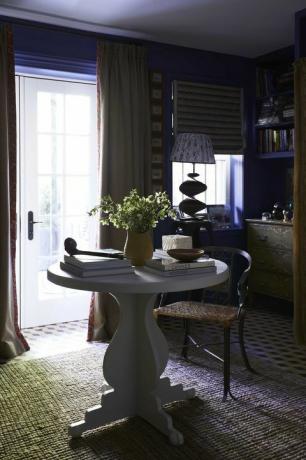 modra dnevna soba, modro poslikana stena, bela okrogla miza, knjige za klubsko mizico