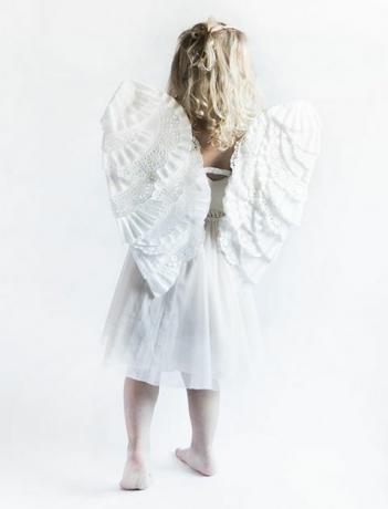 на спині маленька дівчинка в білому платті та крилах ангела