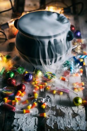 изглед от висок ъгъл на тенджера с дим сред разпръснати бонбони на масата по време на Хелоуин