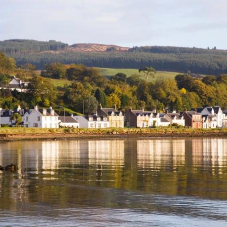 casas frente al mar se refleja en las tranquilas aguas de lamlash bay, isla de arran