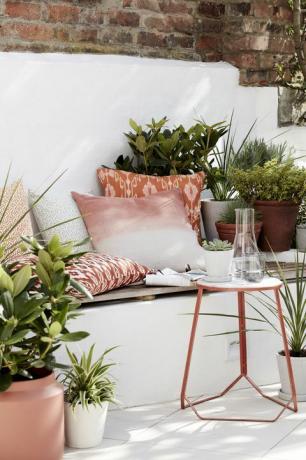 haveideer, udendørs siddeområde fyldt med hynder, planter og et sidebord
