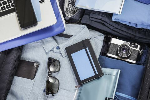 Dettaglio sopraelevato della valigia imballata con camicia blu, fotocamera retrò, laptop, smartphone e notebook