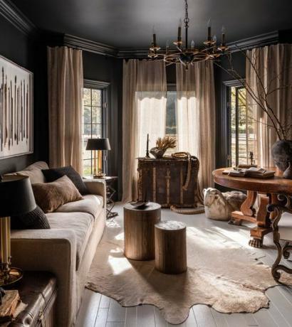 Wohnzimmer, Teppich aus Tierhaut, Holzboden, runde Couchtische aus Holz, schwarz gestrichene Wände