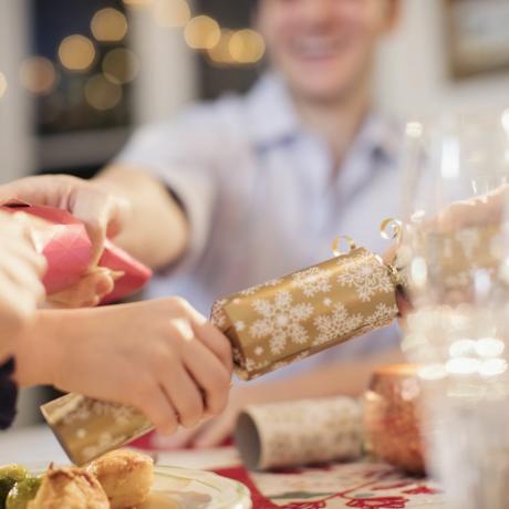 Rodzina ciągnąca świąteczne krakersy przy stole