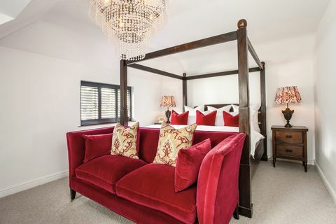 Weißes Schlafzimmer mit Himmelbett und rotem Sofa