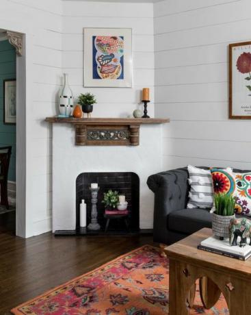 obývací pokoj, dřevěná podlaha, koberec, dřevěný konferenční stolek, kachlový krb v bílém a černém metru, tmavě šedá pohovka s barevnými polštáři