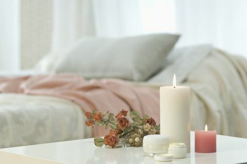 Sviečky, pleťový krém a zväzok ruží na stole s posteľou