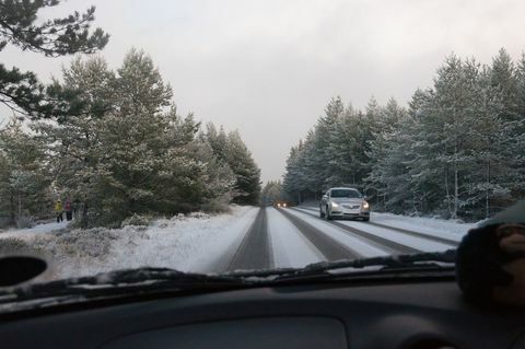 Un coche circula por una carretera cubierta de nieve entre árboles