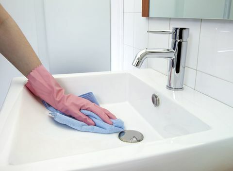 Waschbecken reinigen: Die Frau, die das Waschbecken mit Mikrofasertuch und Handschuhen reinigt