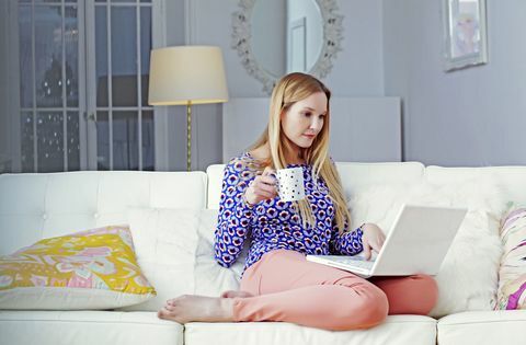 Moteris ant nešiojamojo kompiuterio sėdi savo svetainėje