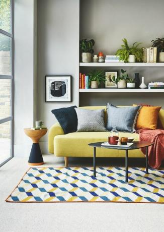 sala de estar, sofá amarillo, estante blanco detrás con una alfombra estampada azul y amarilla en el piso