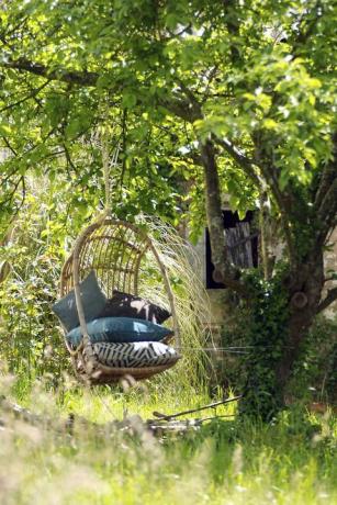 Gartenschaukel umgeben von grünem Laub mit einem Haufen Kissen