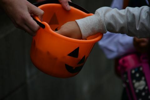 Apgriezts attēls, kurā rokas paņem konfektes no Helovīna groza
