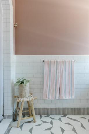 गुलाबी रंग की दीवार, सफेद सबवे टाइल, लकड़ी का मल, सफेद शावर पर्दा, ज्यामितीय सफेद और ग्रे टाइलें, गुलाबी और भूरे रंग के तौलिये