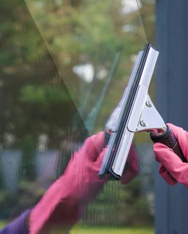 ruku v růžové gumové ochranné rukavice mytí a čištění oken s profesionálně stěrkou předjarní čištění oken na pozadí stromů