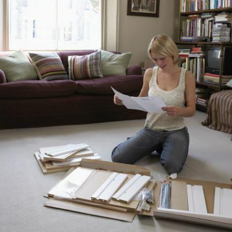 Mulher ajoelhada no chão da sala de estar lendo as instruções para montar a mobília flatpack
