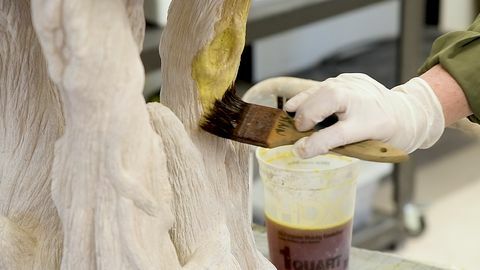 Imagen de primer plano medio de una mano enguantada aplicando tinte ácido a una escultura con capas de fibrocemento