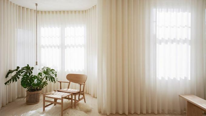 Schlafzimmer Londoner Niedrigenergiehaus mit drapierten Vorhängen über Erkerfenster, Akzentstuhl und großer Pflanze