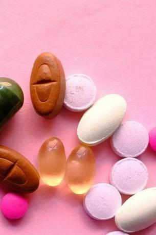 Įvairios farmacinės medicinos tabletės, tabletės ir kapsulės rožiniame fone