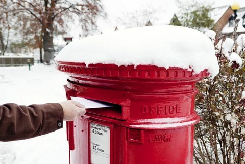 Uomo che spedisce una lettera in una buca delle lettere britannica coperta di neve