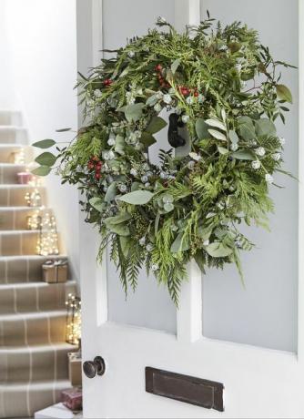 إكليل عيد الميلاد على الباب الأمامي الأبيض مع الأضواء على طول الدرج