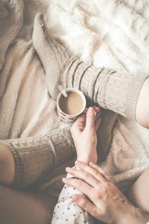 Weibliche Beine in Stricksocken mit Tasse Kaffee