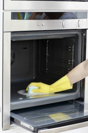 Kvinne iført gul oppvaskhanske for å rengjøre innsiden av ovnen med svamp