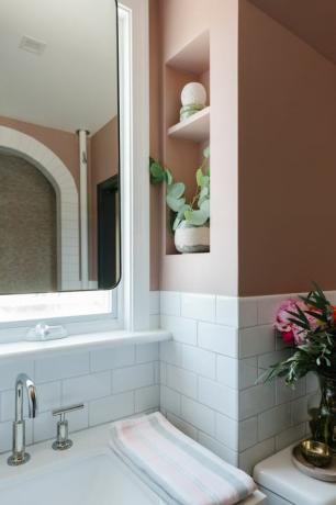 białe płytki metra, ściany pomalowane na różowo, srebrny kran, lustro, wbudowane półki, różowe i szare ręczniki do rąk