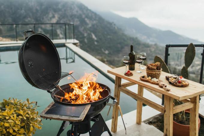 подготовка к роскошной вечеринке барбекю на открытом воздухе, горящий огонь в гриле, стол с закусками и вином