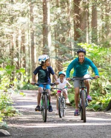 en kvinna och hennes två barn cyklar i skogen i solskenet