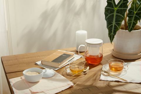 klares Teeservice neben Buch, Pflanze, Diffusor und Glas auf Holztisch